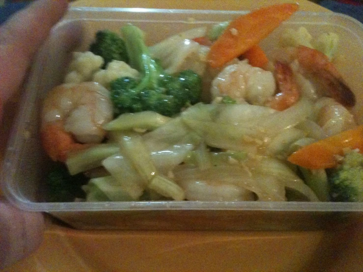 a plastic container that has some broccoli and shrimp in it