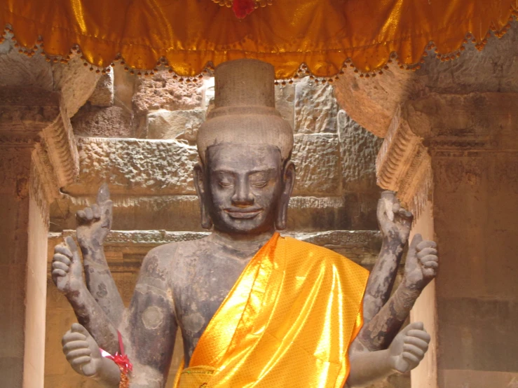 a statue in a yellow and orange outfit holding up some palm fronds