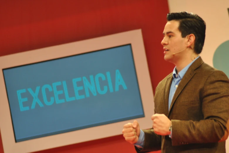 man standing next to a large screen displaying a word with the word ex excellence