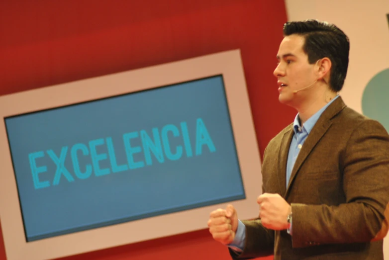 man standing next to a large screen displaying a word with the word ex excellence