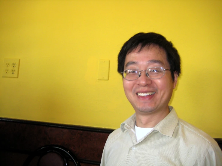 a smiling man wearing glasses in front of yellow walls