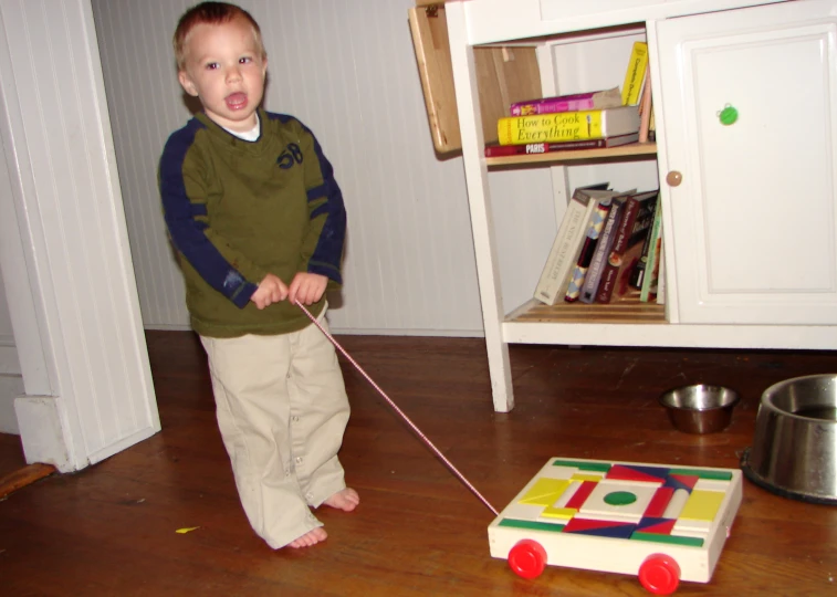 a child pulls his toy car on a wooden floor