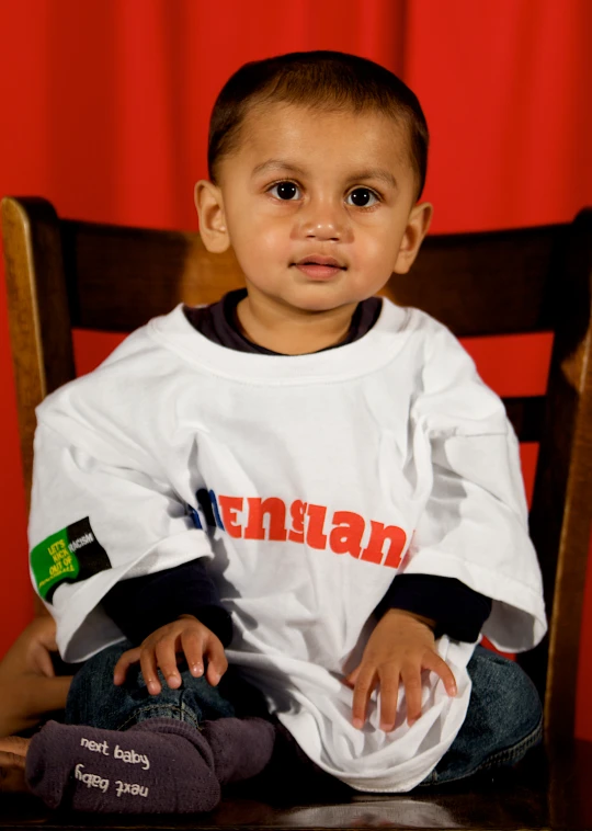 a small child with short black hair is sitting in a chair