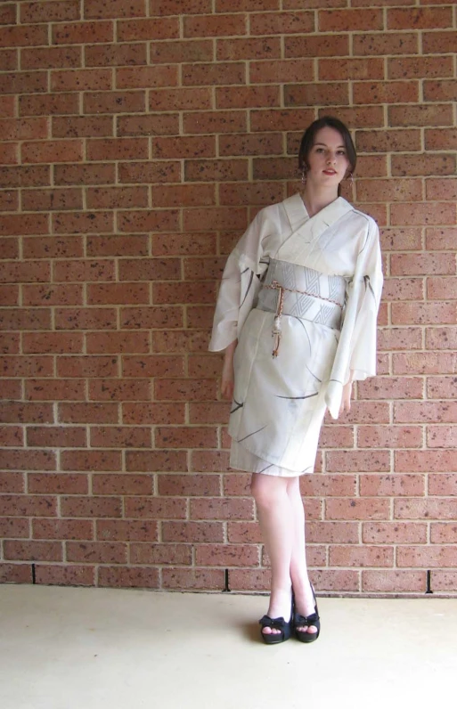 a woman wearing a white dress and shoes, leaning against a brick wall