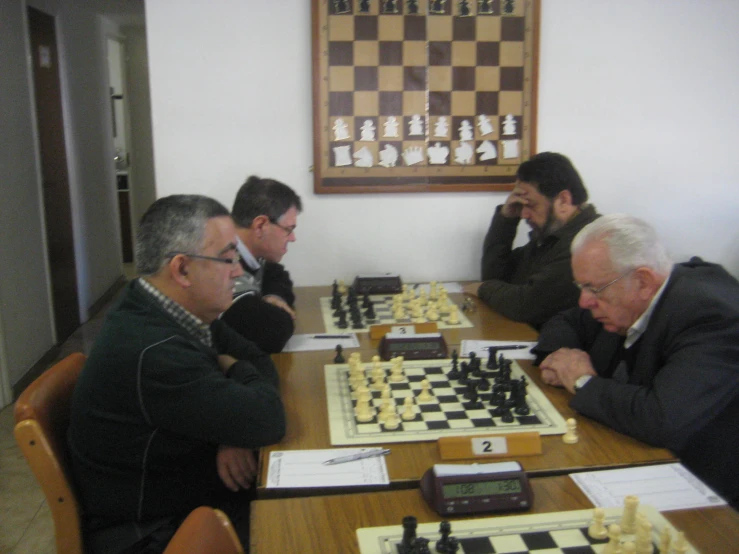 four men playing chess together at a large table