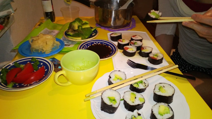 a yellow table topped with plates and bowls filled with sushi