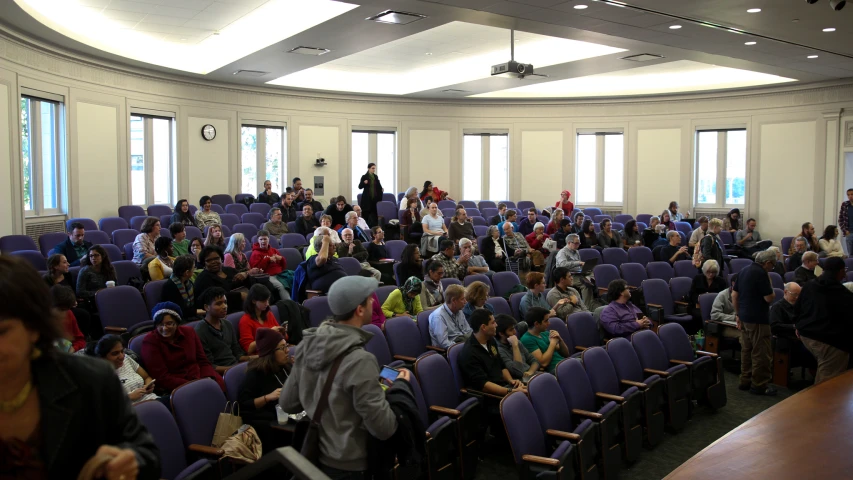 a crowd of people sit inside of chairs with windows in the room