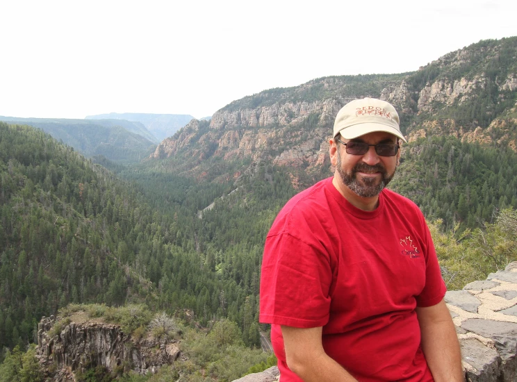 man in red shirt sitting on top of a cliff