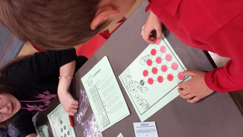 two boys and a girl sit at a table with paper work