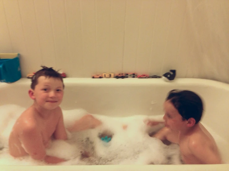 two boys sit inside a bath tub full of foam