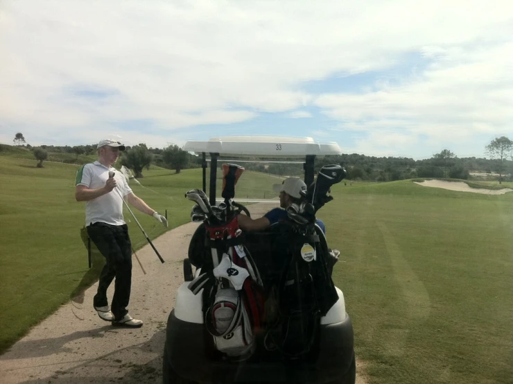 two men standing near a golf cart with some golf clubs