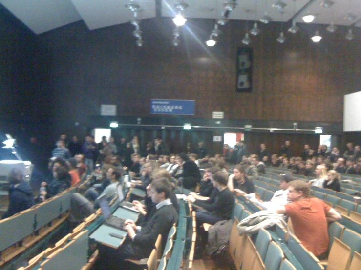 some students are sitting in the auditorium with their laptops