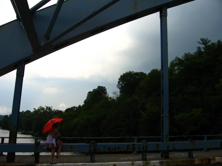 woman with umbrella walking on bridge near river