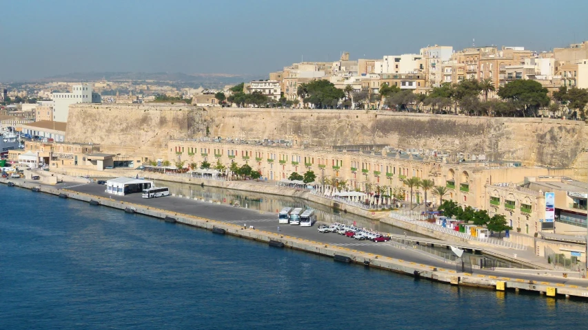 cars and trucks are parked along the water of a harbor