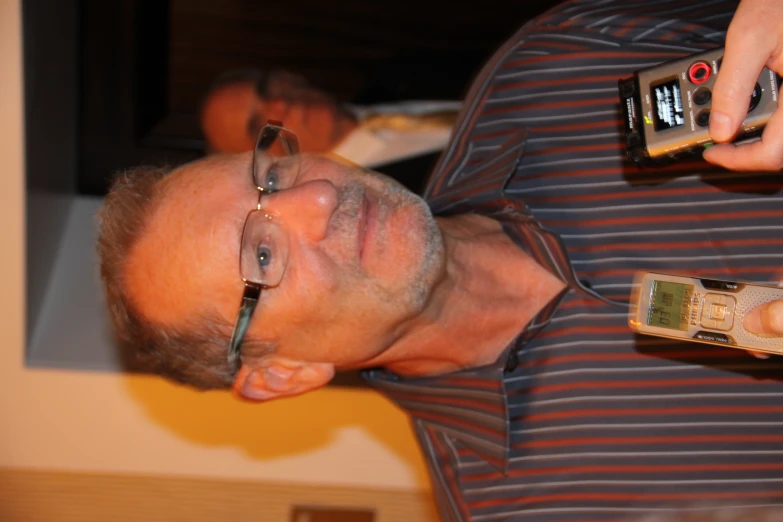 man in striped shirt holding up 2 different cell phones