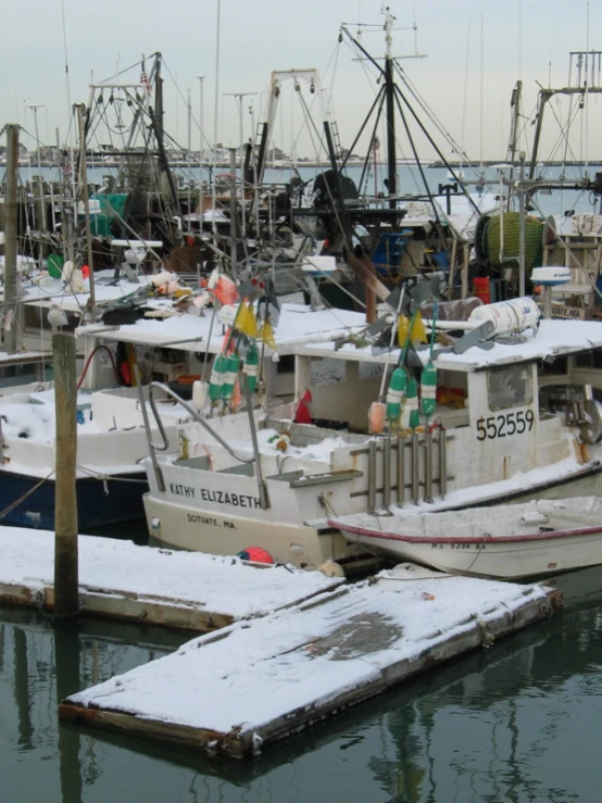 several boats tied to the docks with snow on them