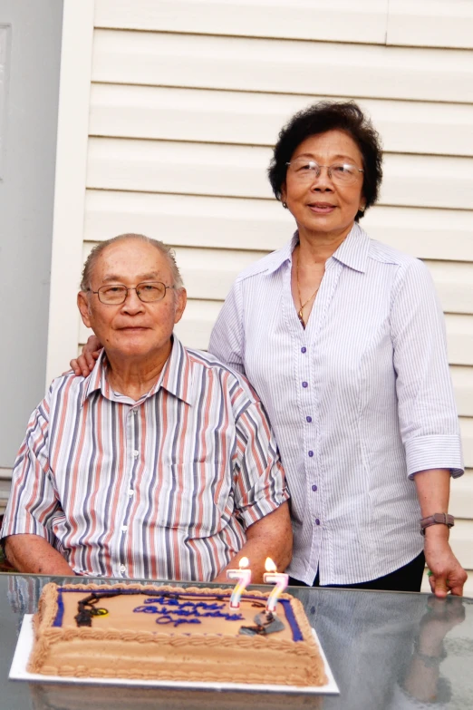 an older man and young woman standing by a cake with candles