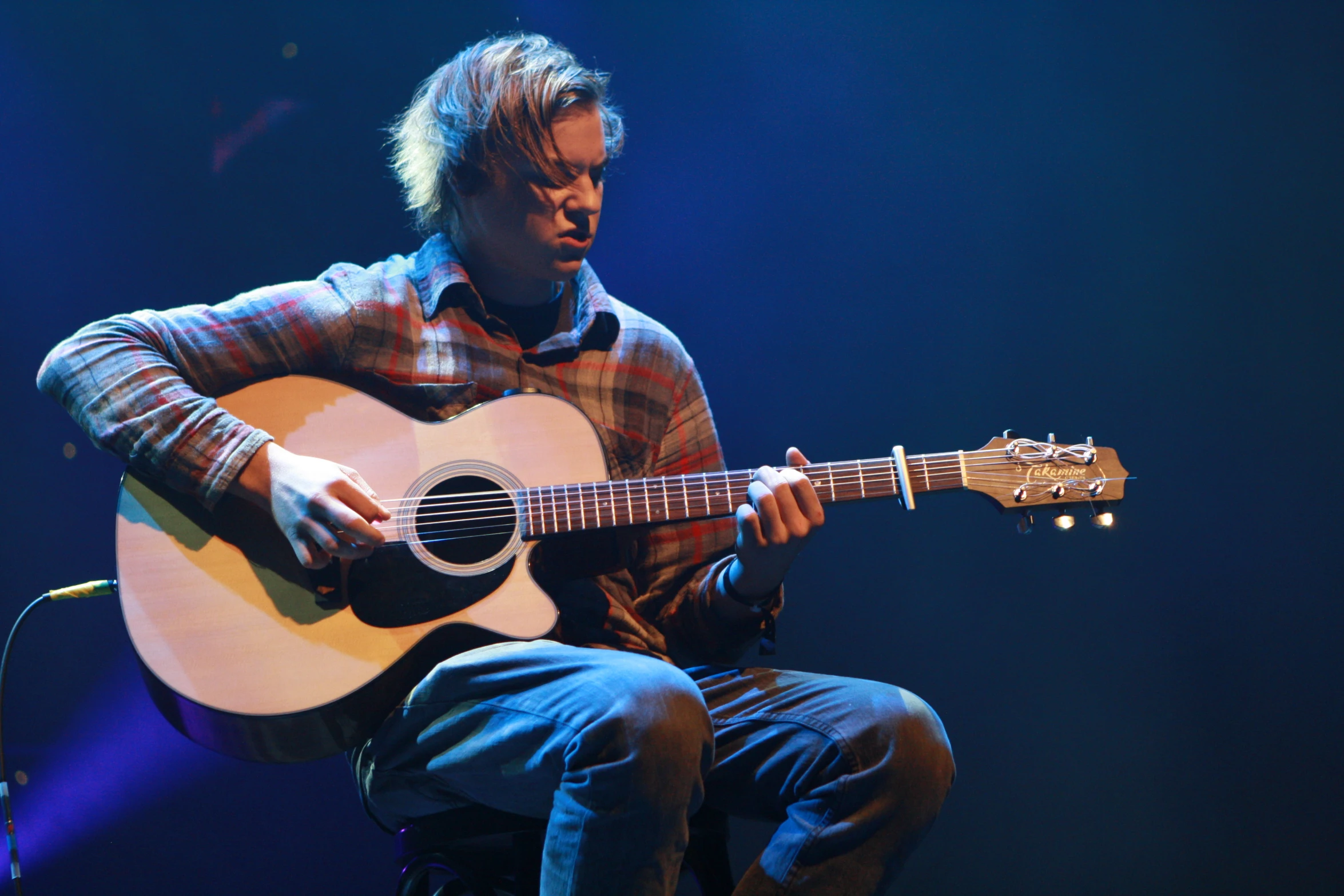 a man with an acoustic guitar sitting on stage