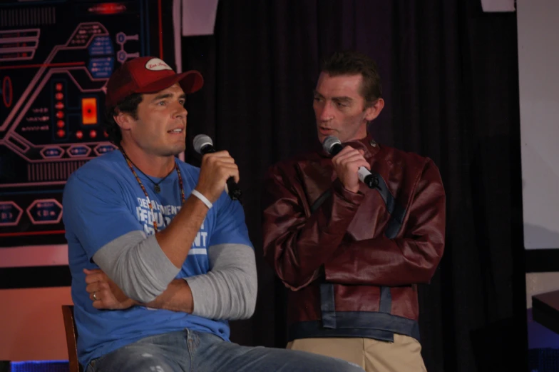 two men are speaking into microphones in front of a stage