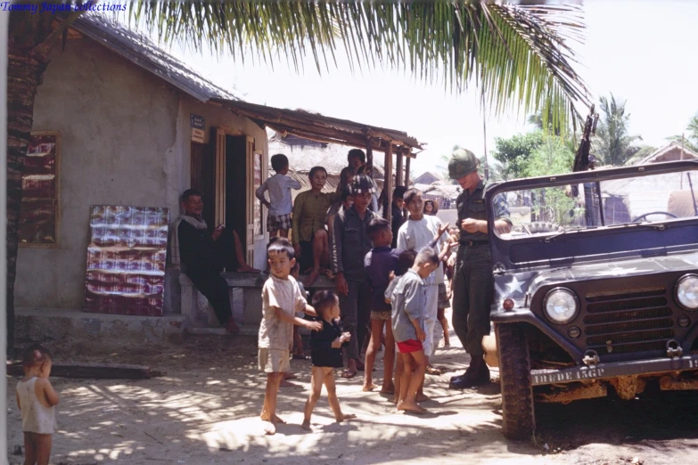 a group of people and an old jeep in front of some houses