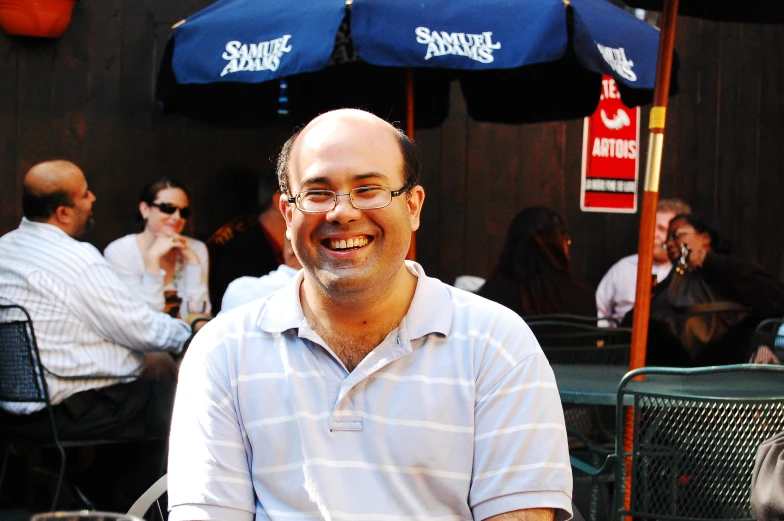 a smiling man sitting at an outdoor table