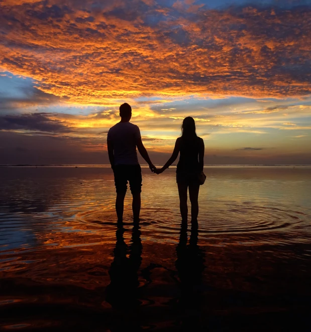 two people hold hands while standing in the water