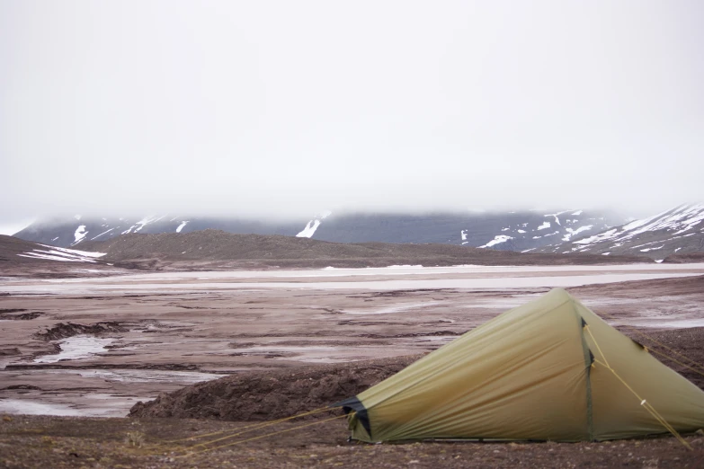 a yellow tent set up in the desert near snow covered mountains