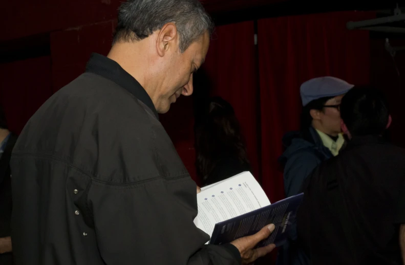 a man holding a book while standing in front of a red curtain