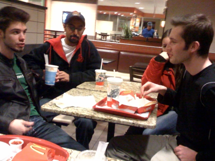 four young men sitting at a table talking to each other