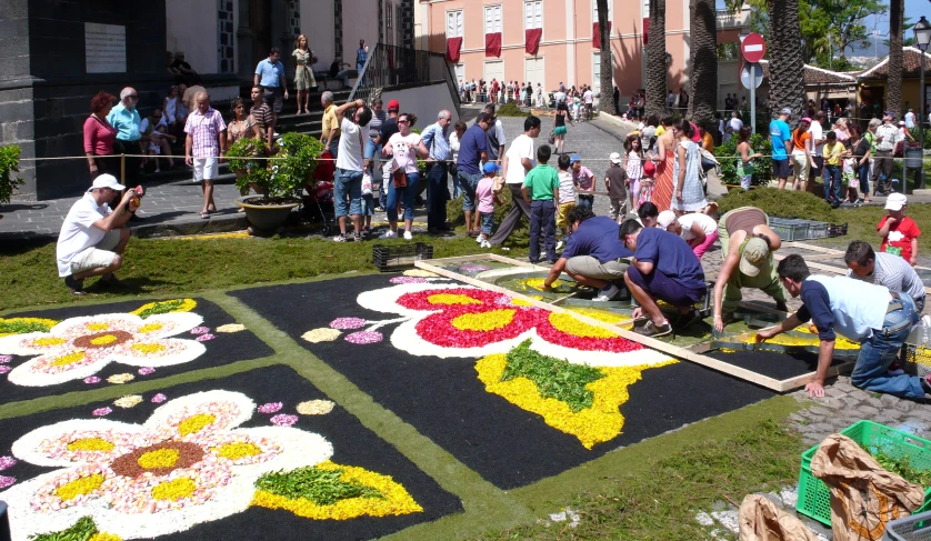 people looking at a carpet with flowers on it in front of a building