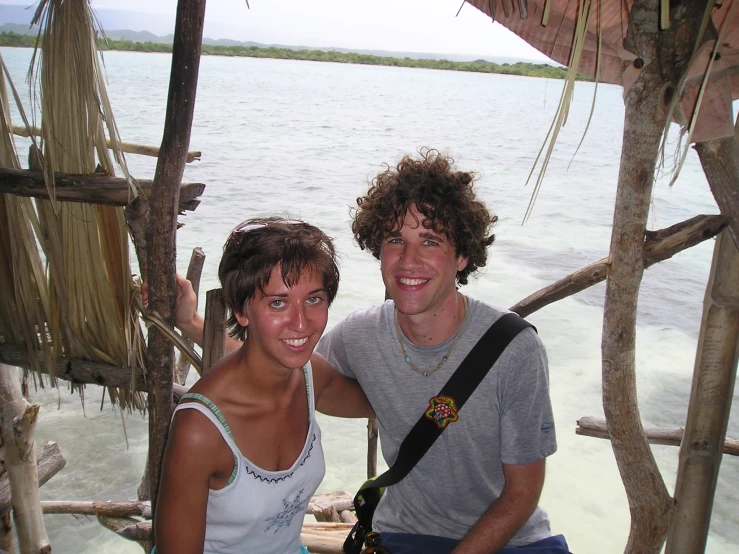 two people smile for the camera while posing with a body of water behind them