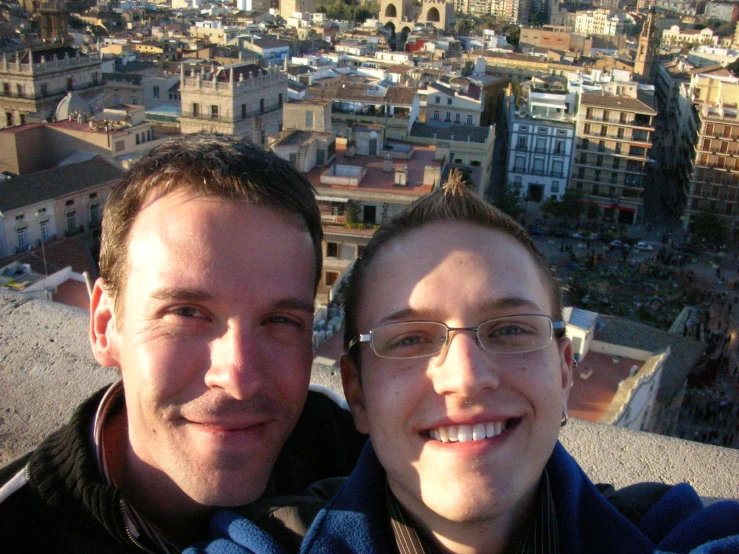 two men taking selfies with a view of city buildings