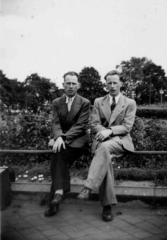 two men sitting on a metal bench in front of trees