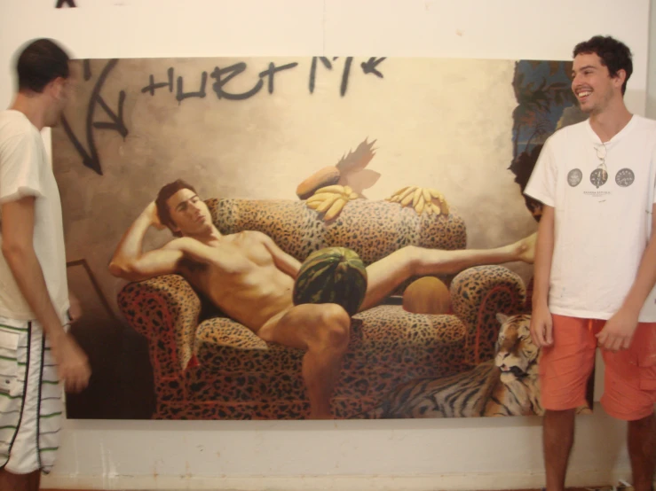 a couple of men standing near a painting of a man on a couch