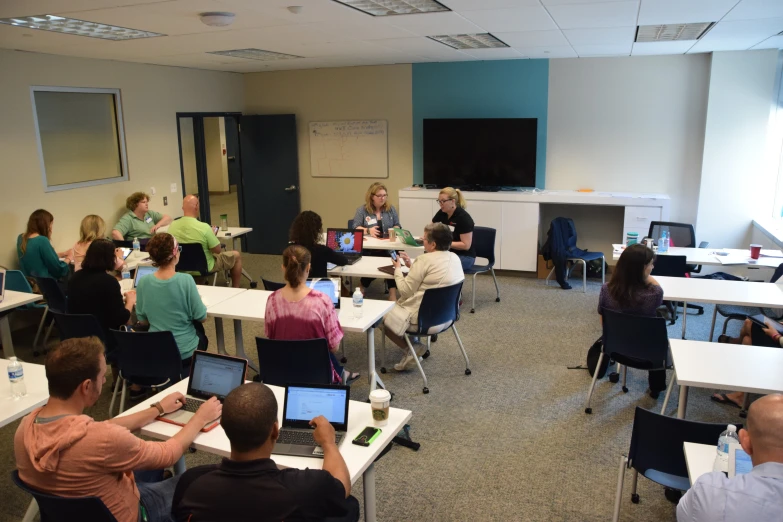 a classroom with people sitting in chairs and facing the class