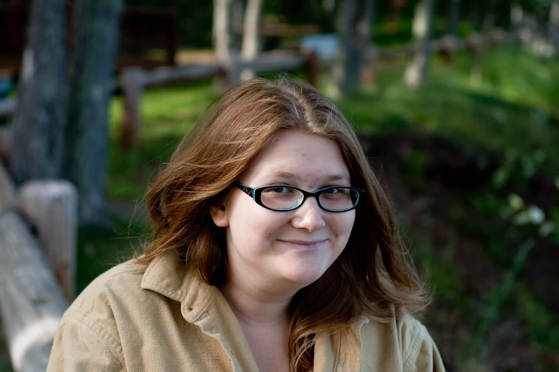 a woman wearing glasses standing in front of some trees