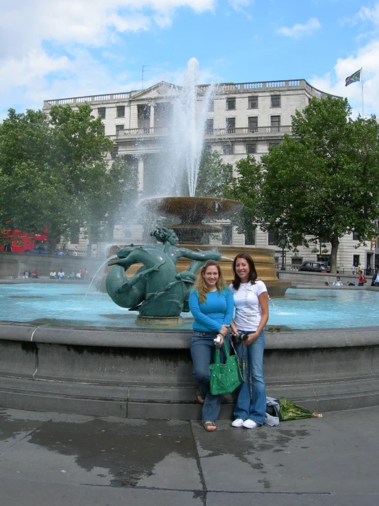 two ladies standing in front of a fountain in the city