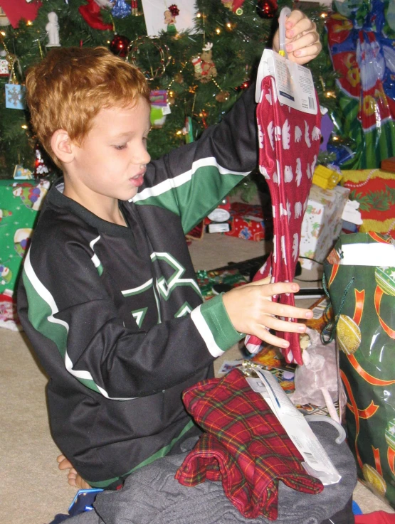 a boy in pajamas holds up his present under a christmas tree