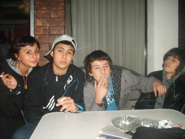 four friends sitting at a table together smoking