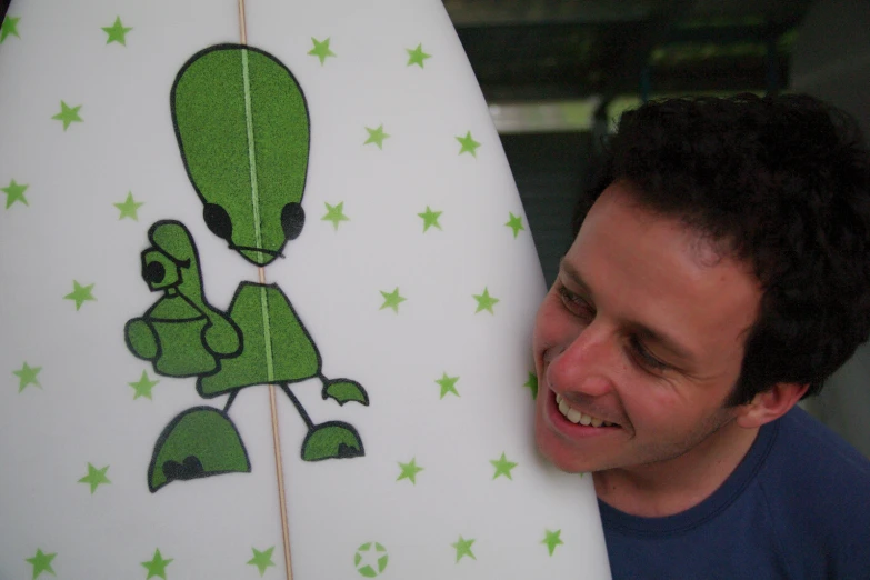 a man holding his surfboard with the green aliens on it