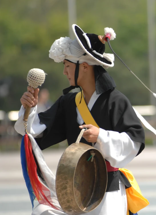 a man in oriental garb plays a beatle drum and a large piece of drum