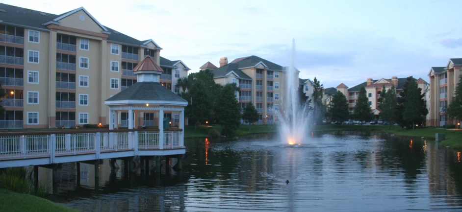 a pond with an artificial fountain and buildings in the background