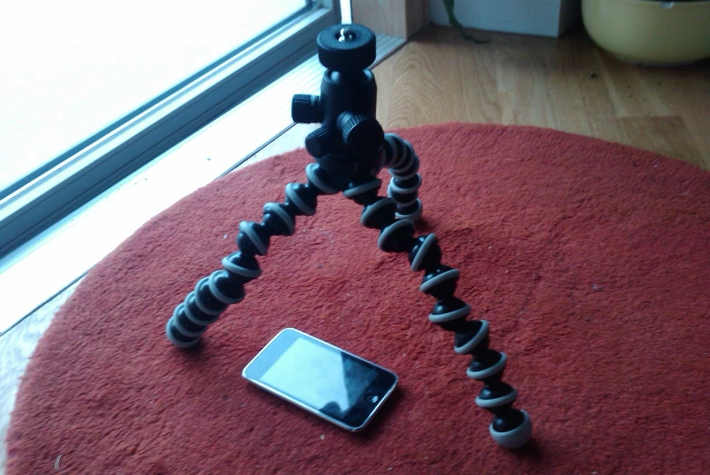 a camera tripod sitting on top of a rug next to a smart phone