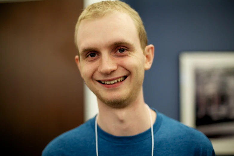 man with earbud on in blue shirt smiling for the camera