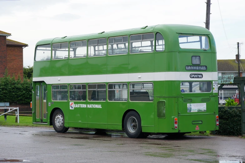 a green double decker bus parked next to a red house