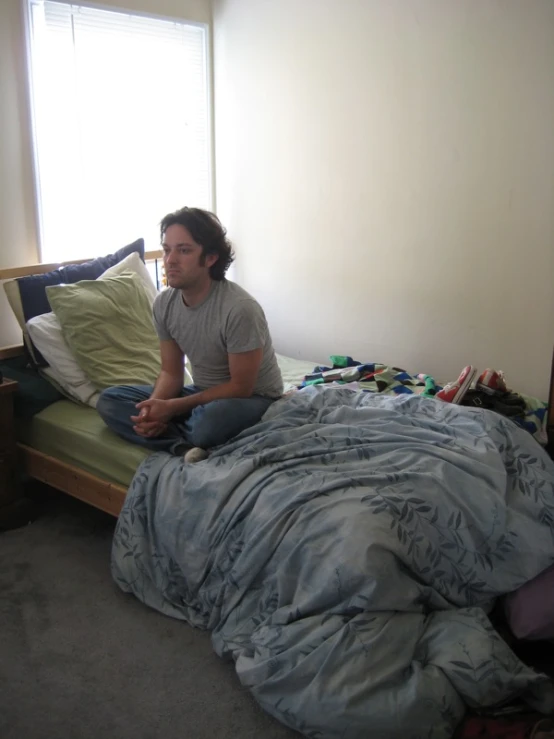 a man sits on an unmade bed in a room