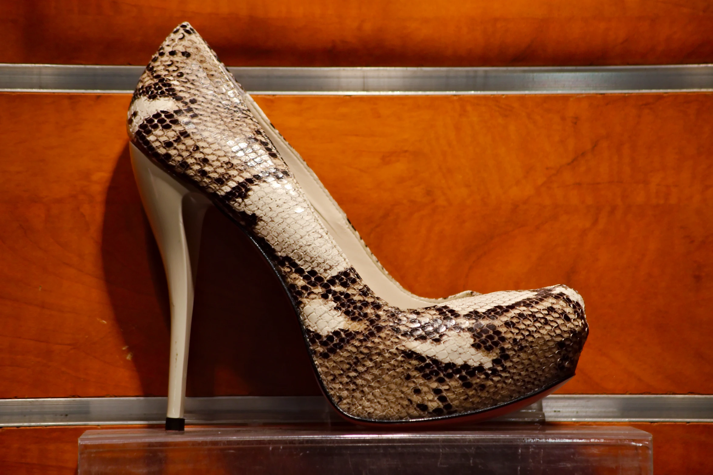 the bottom part of a high heeled shoe is in an area that has brown and white patterned leather