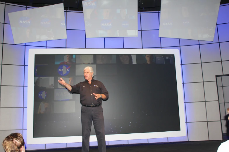 an older man giving a lecture on a large screen