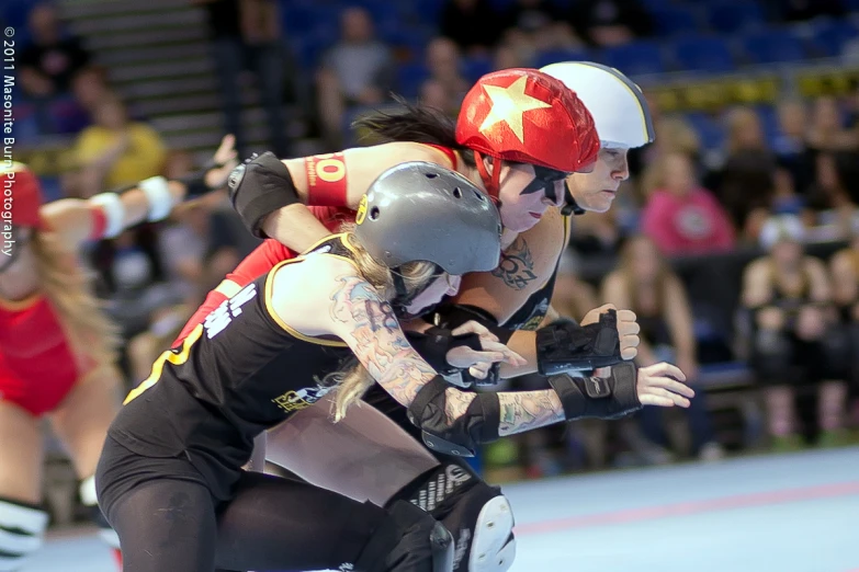 two women wrestling in a indoor race wearing helmets and gloves