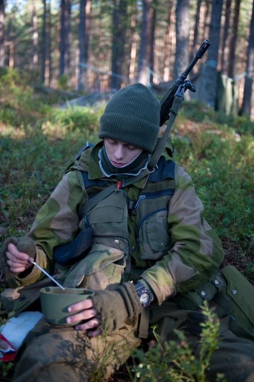 a young man sitting in the woods holding his hunting gear